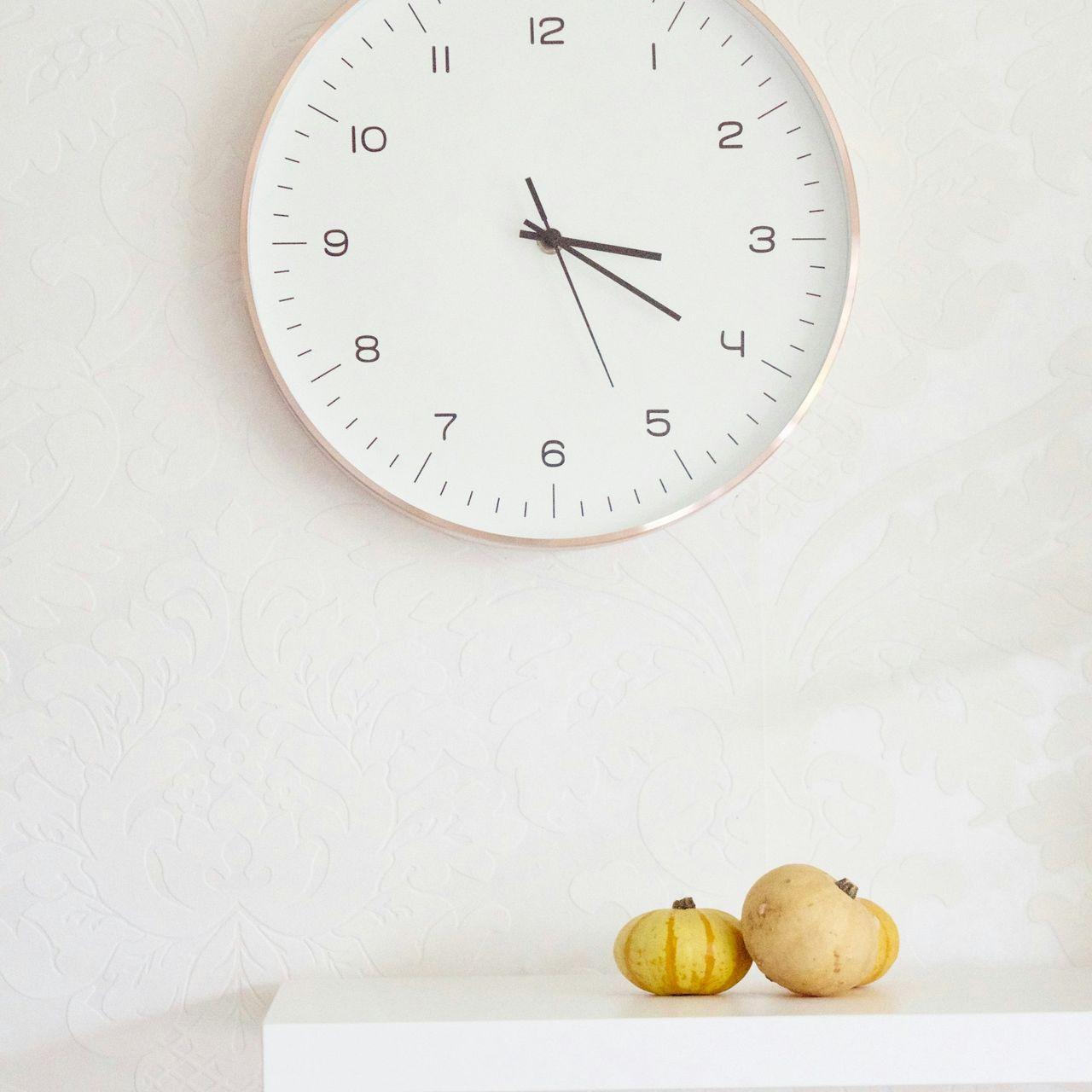 two pumpkins on table below wall clock