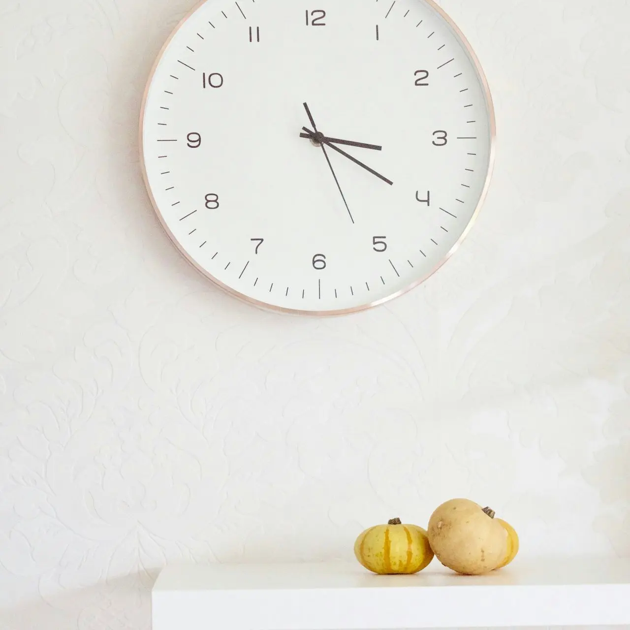 two pumpkins on table below wall clock